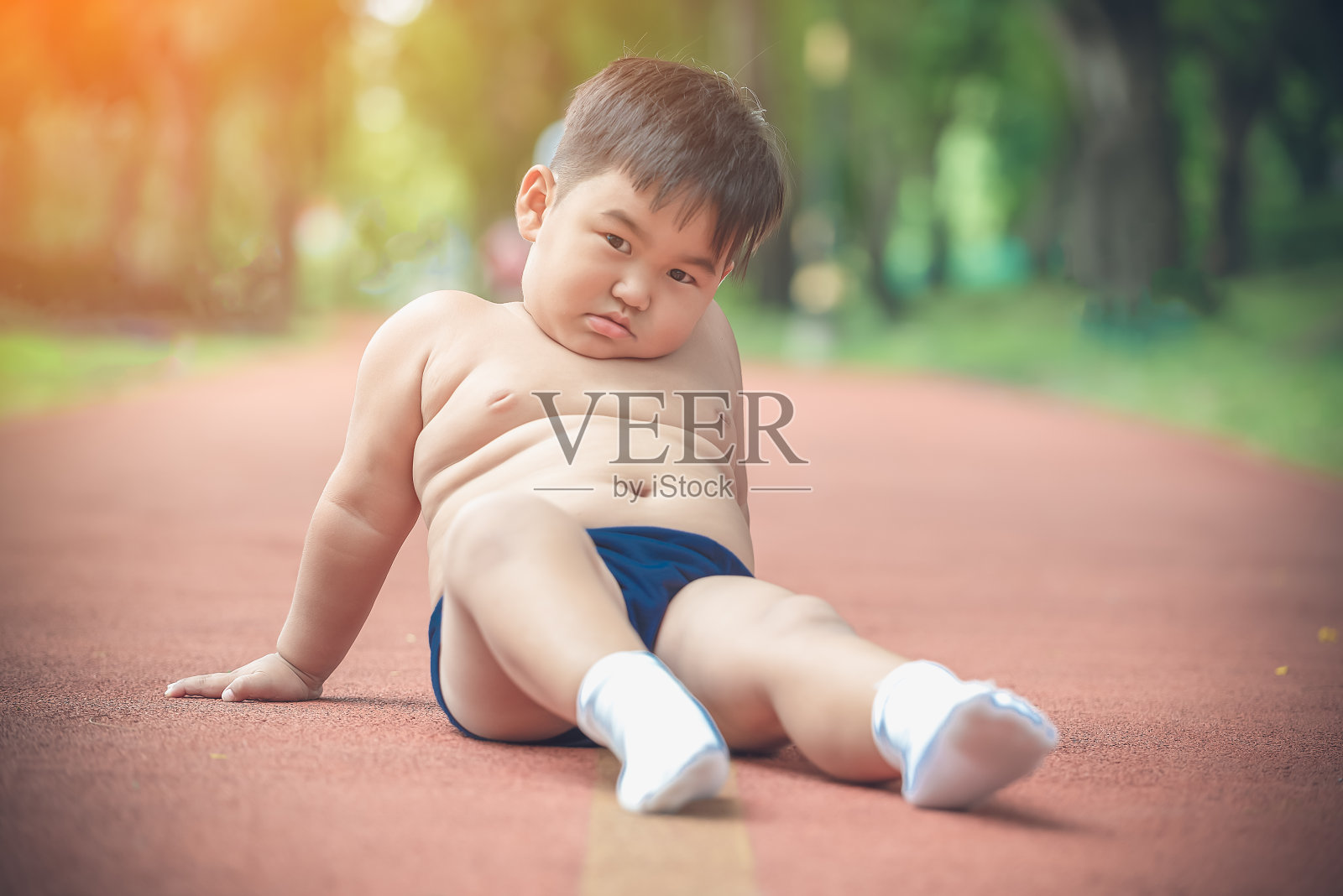 疲惫的胖男孩坐在跑步道公园上照片摄影图片