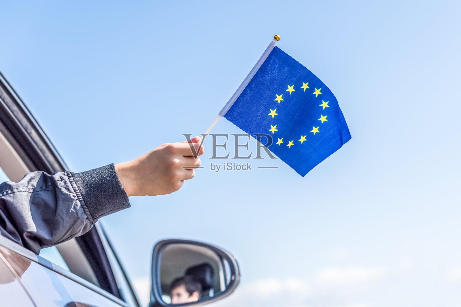 在天空的背景中,一个男孩从打开的车窗中拿着欧洲或欧盟的旗帜。的概念。照片摄影图片