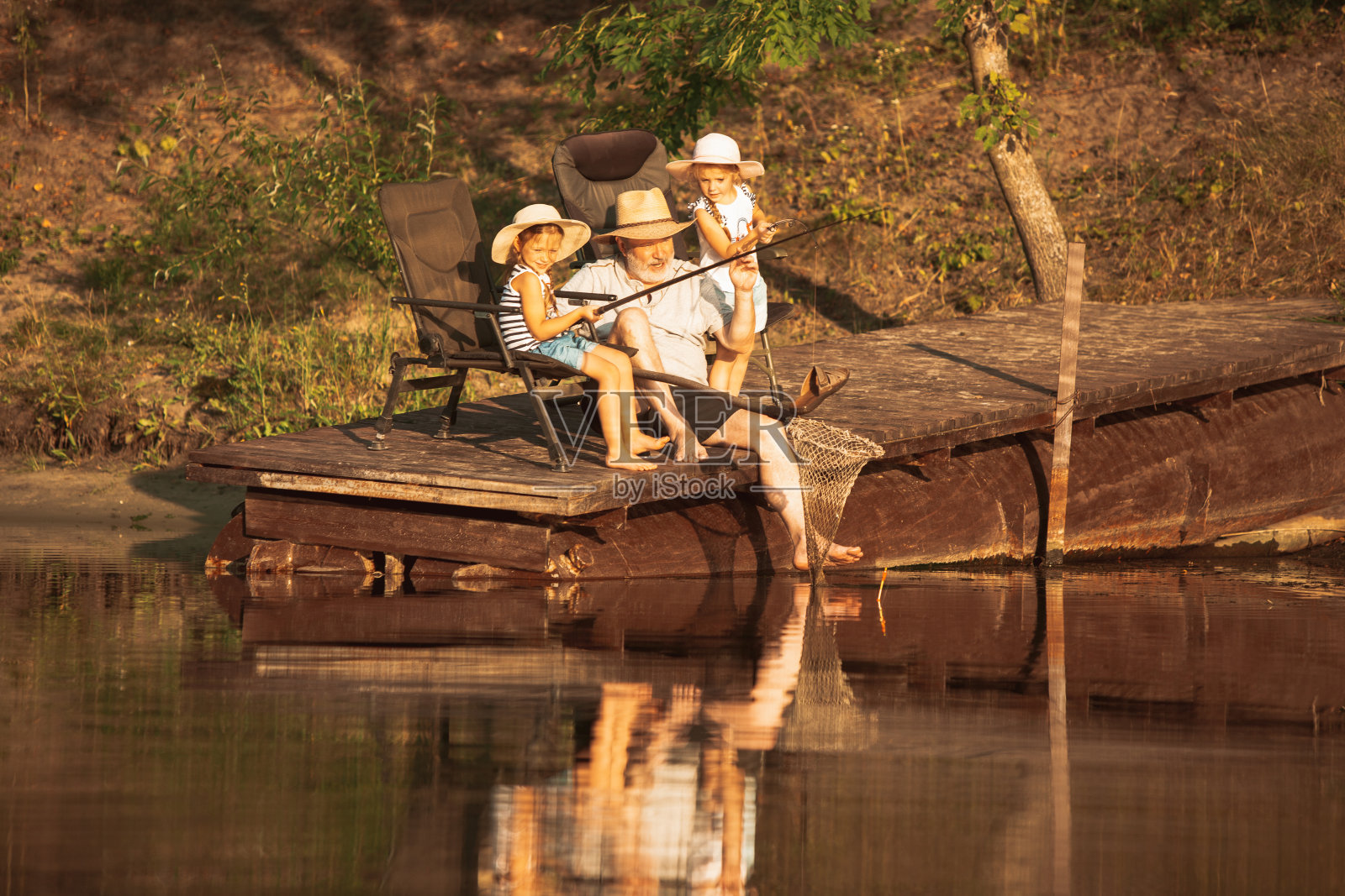 可爱的小女孩和他们的爷爷在湖边或河边钓鱼照片摄影图片