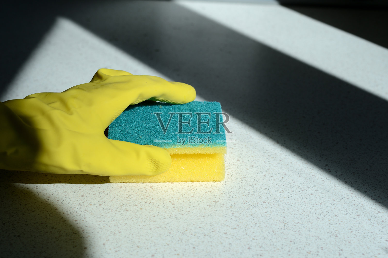 手拿黄色橡胶手套清洗被阳光照射的厨房表面。家里清洁照片摄影图片