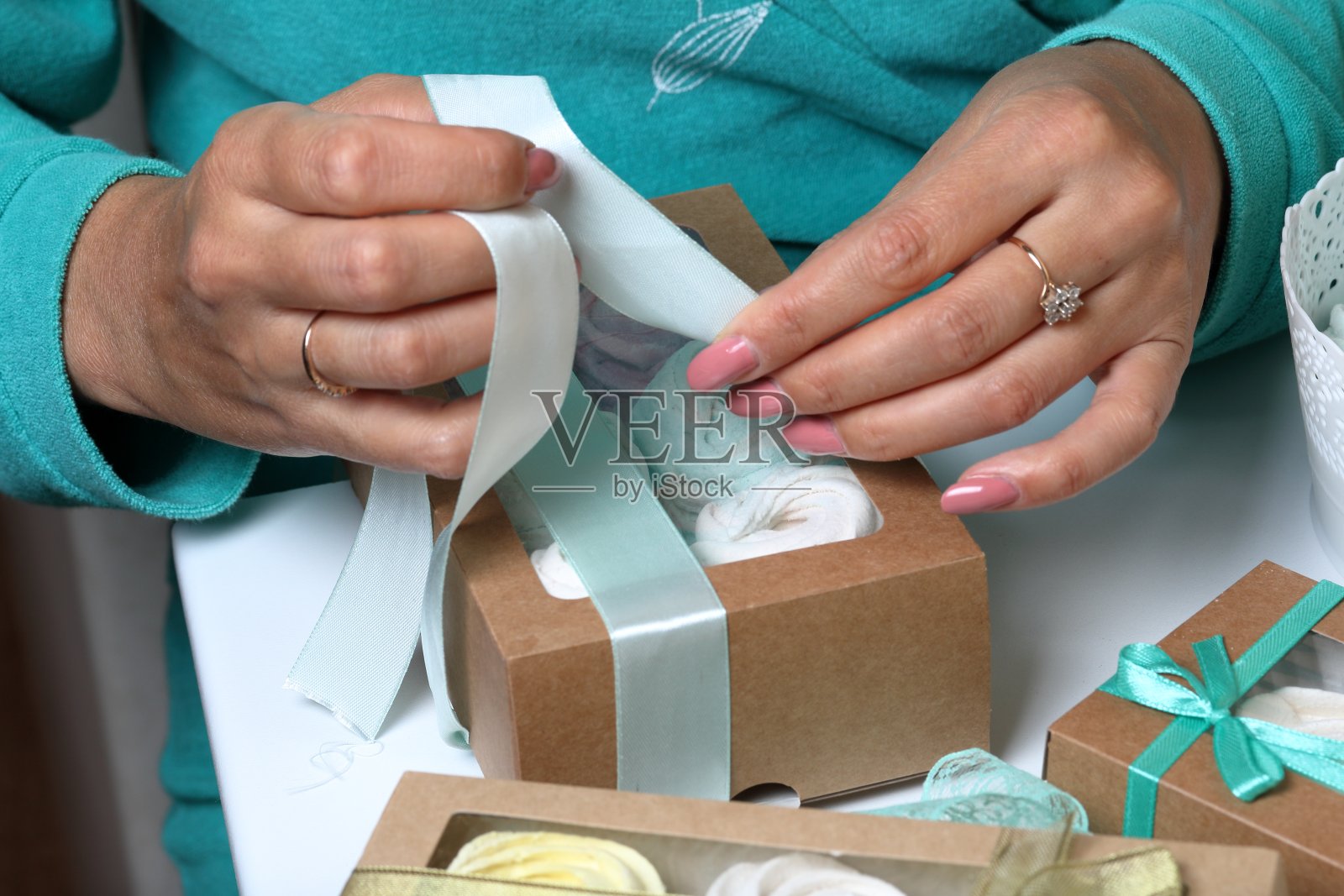 女人把不同颜色的棉花糖放进礼品盒里。用彩色缎带包扎盒子。照片摄影图片