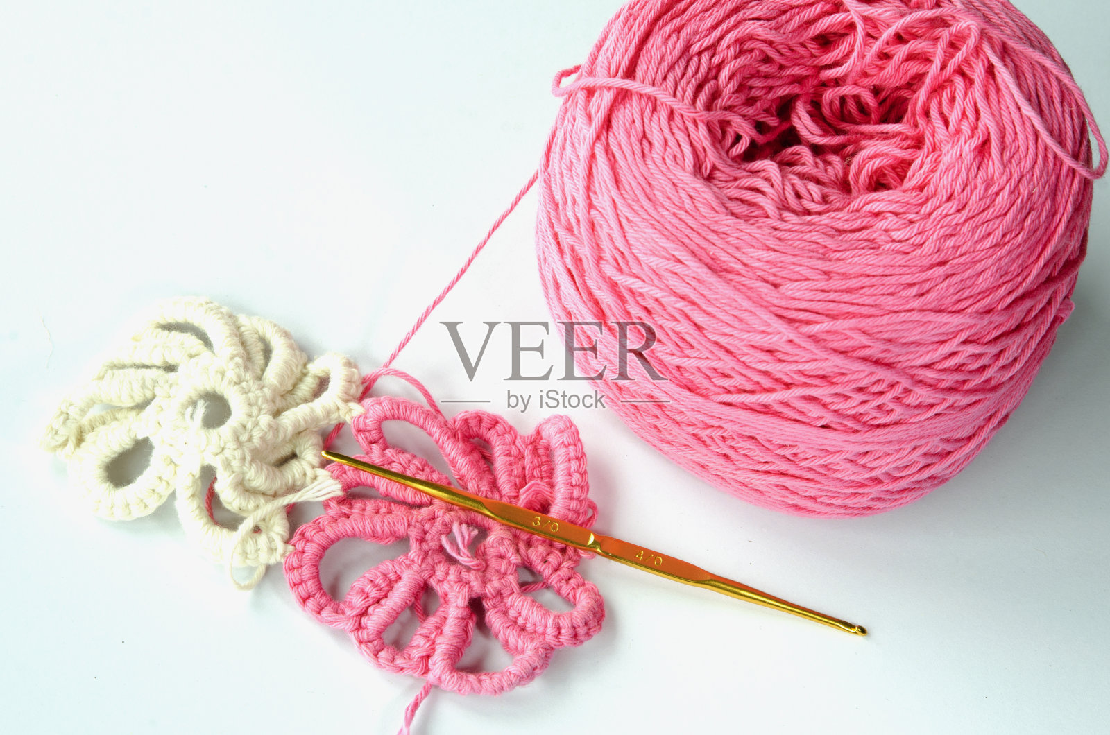 粉红色和白色的棉纱手工钩针花,爱好工艺品钩针与钢钩,白色背景照片摄影图片