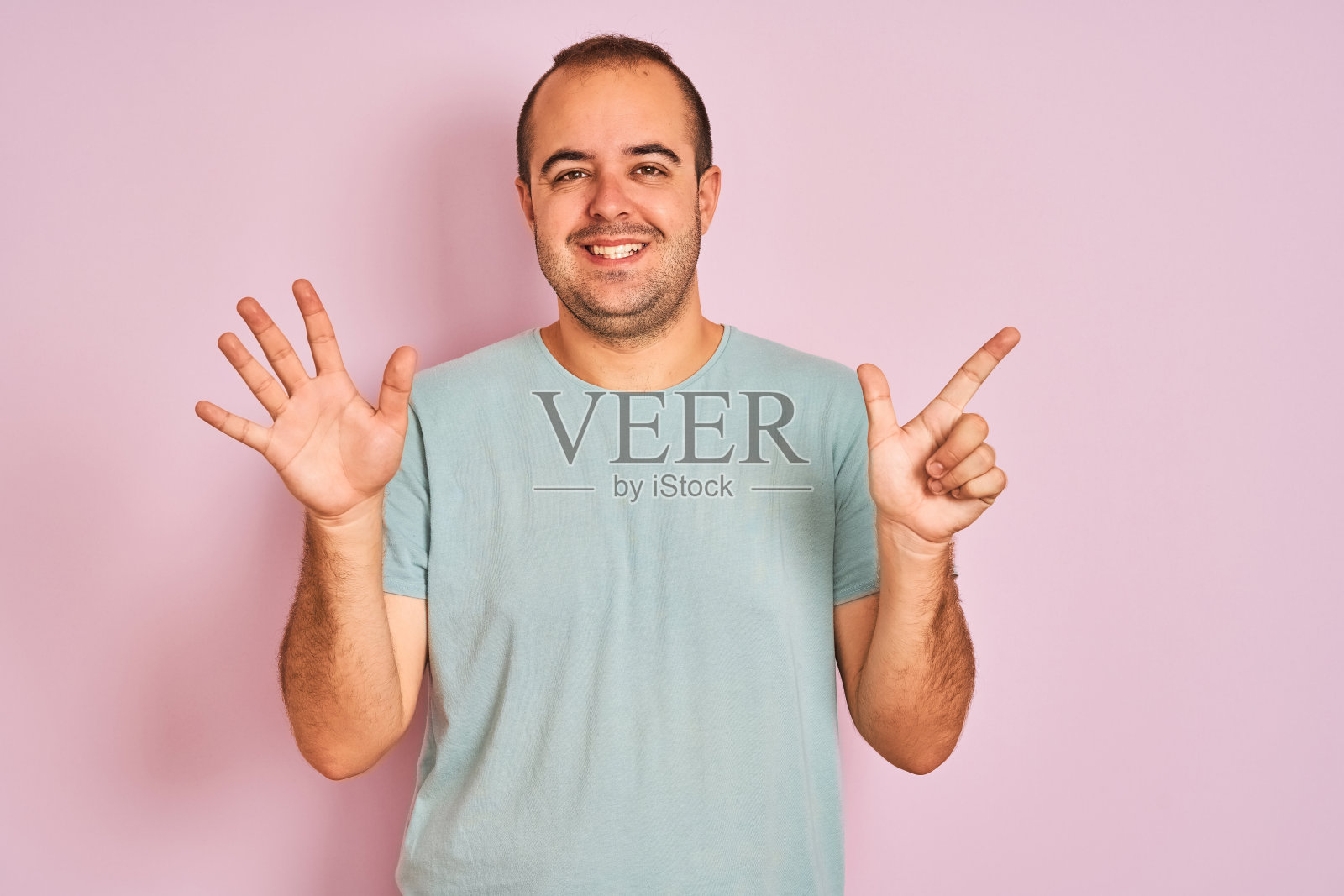 年轻男子穿着蓝色休闲t恤站在孤立的粉红色背景显示和指向数字7,同时自信和快乐的微笑。照片摄影图片