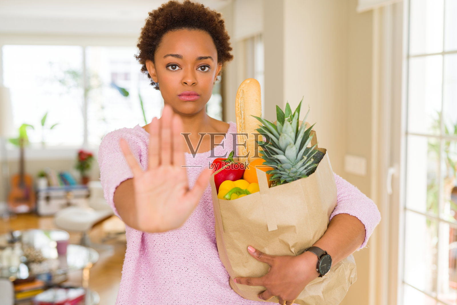 年轻的非洲裔美国妇女拿着装满新鲜食品的纸袋与开放的手做停止标志与严肃和自信的表情,防御手势照片摄影图片