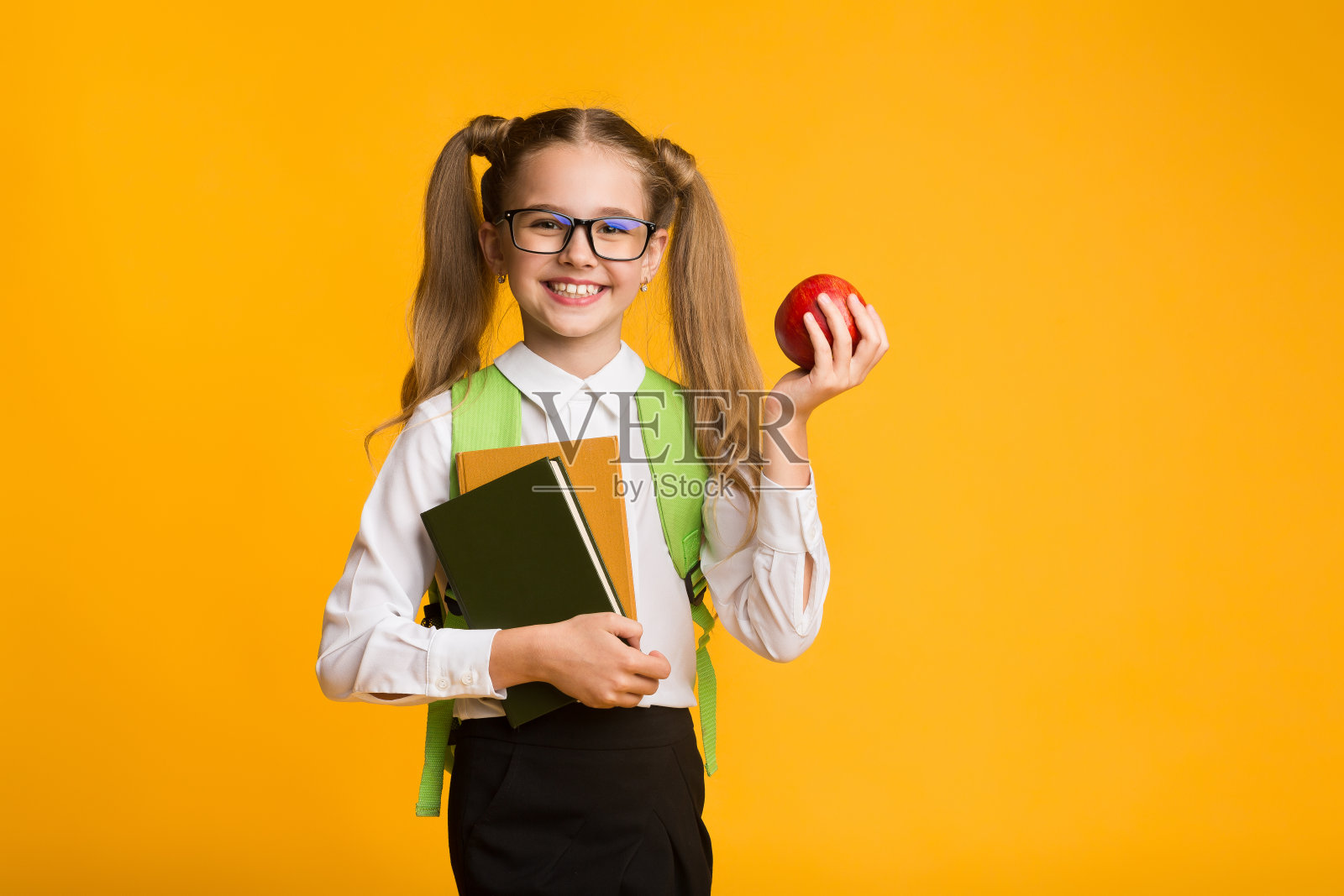 小女孩拿着苹果和黄色背景的书照片摄影图片