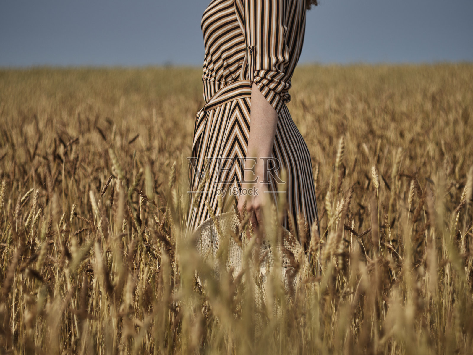 特写镜头中,一个穿着条纹连衣裙的女孩手里拿着一顶草帽照片摄影图片