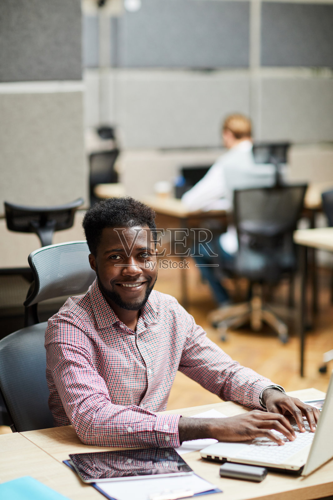 一个快乐的、有经验的非洲裔经理坐在办公室的桌子旁,在笔记本电脑上打字的肖像照片摄影图片