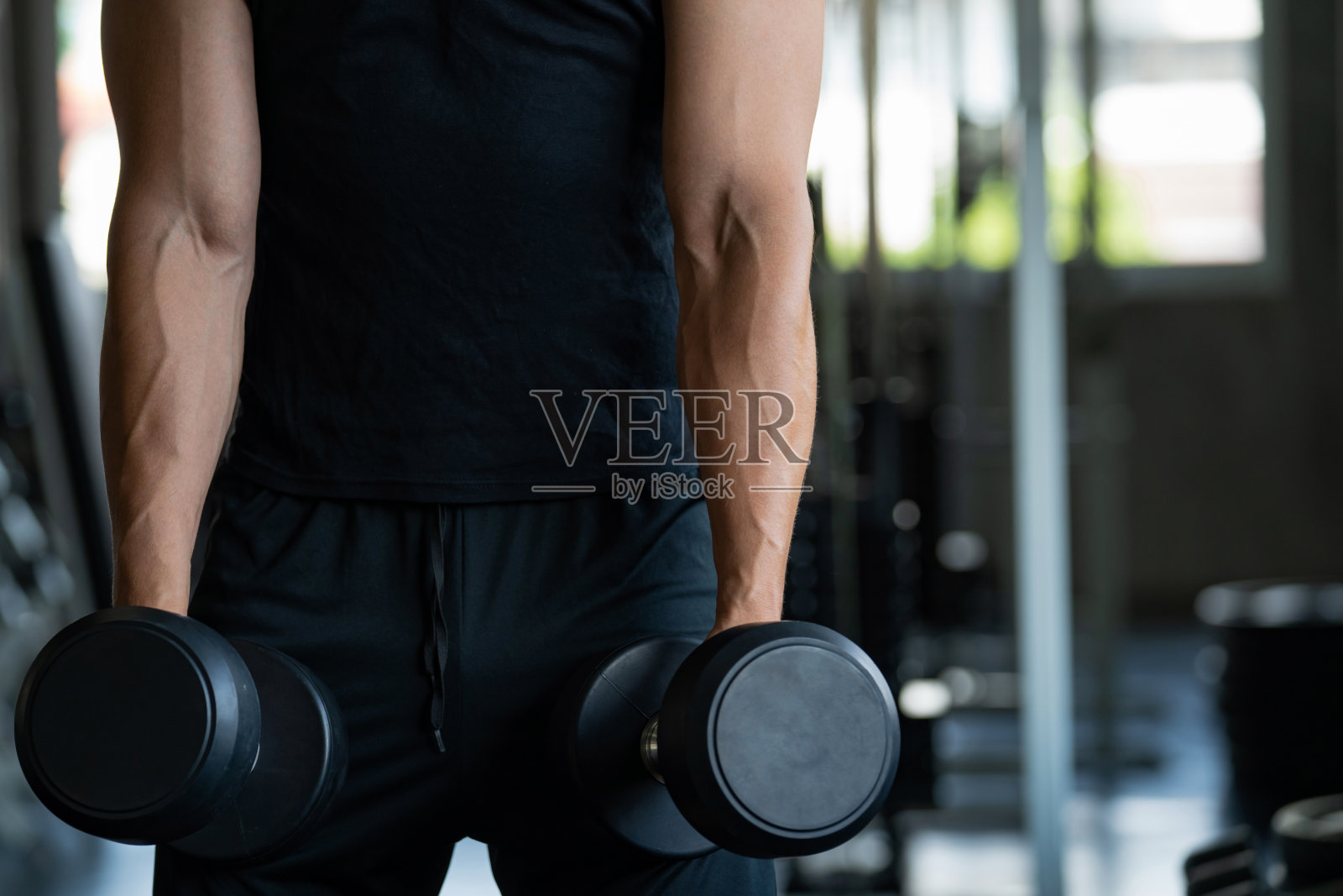 白人健美男在健身俱乐部用哑铃举重。照片摄影图片