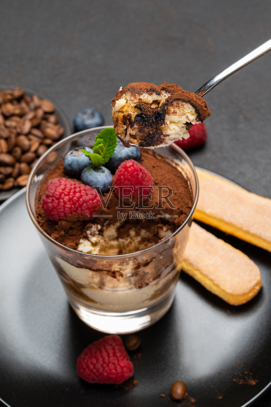 经典的提拉米苏甜点配蓝莓和覆盆子,放在石制的餐板上,背景是混凝土照片摄影图片