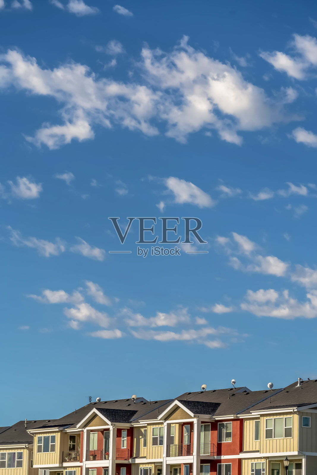 在阳光明媚的日子里,蓝云的天空俯瞰着有着奶油色和红色墙壁的联排别墅照片摄影图片