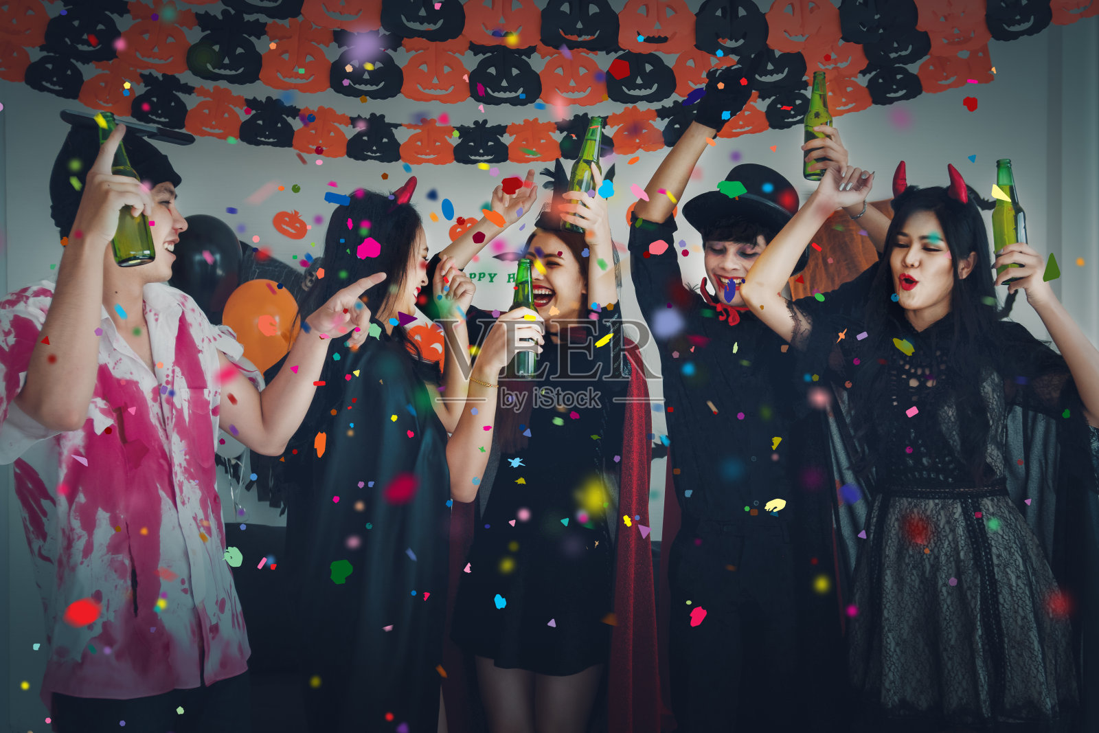 一群亚洲朋友在幽灵服装有乐趣与跳舞和喝啤酒在万圣节庆祝派对照片摄影图片