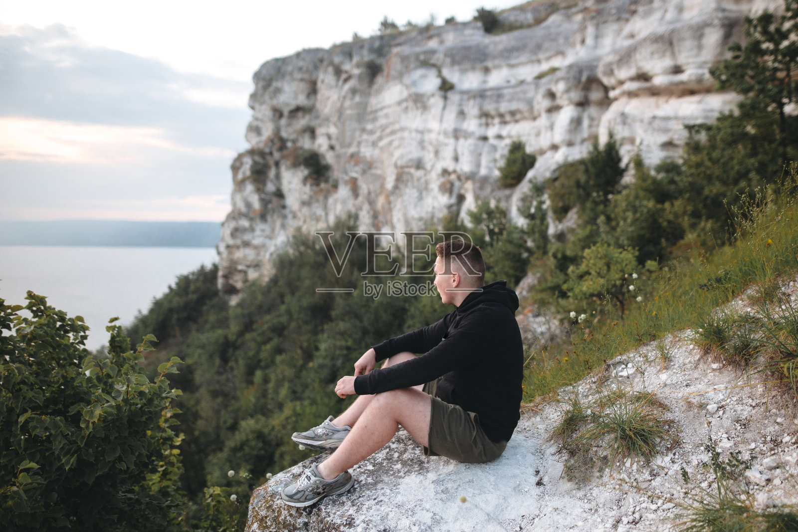 潮人游客坐在岩石山顶,享受惊人的河的景色。穿着风衣探险和旅行的时尚男士。大气宁静的时刻。本空间照片摄影图片