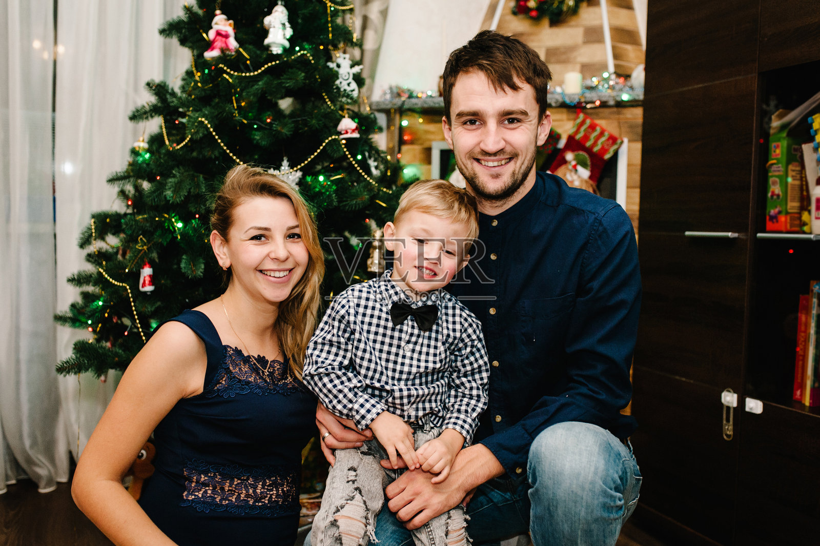 幸福家庭:父母和儿子在圣诞树旁。照片摄影图片