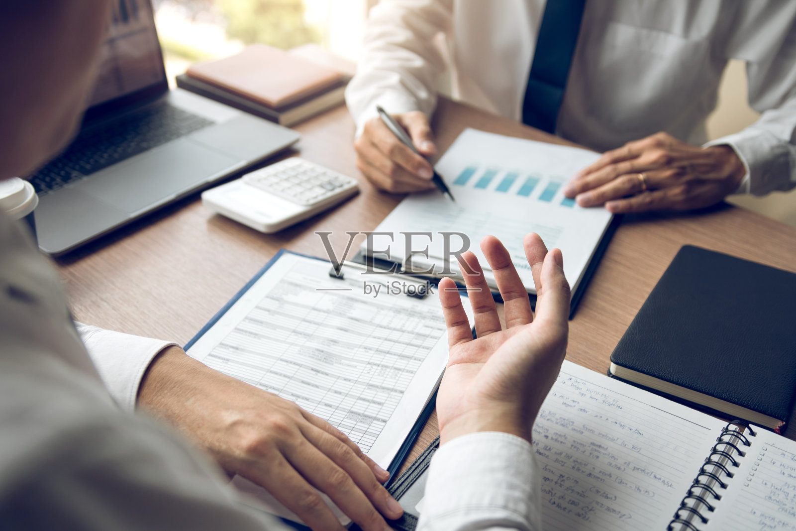 同事们都在强调讨论结果报告总结,并与办公室里的文件纸上的财务信息进行比较。照片摄影图片