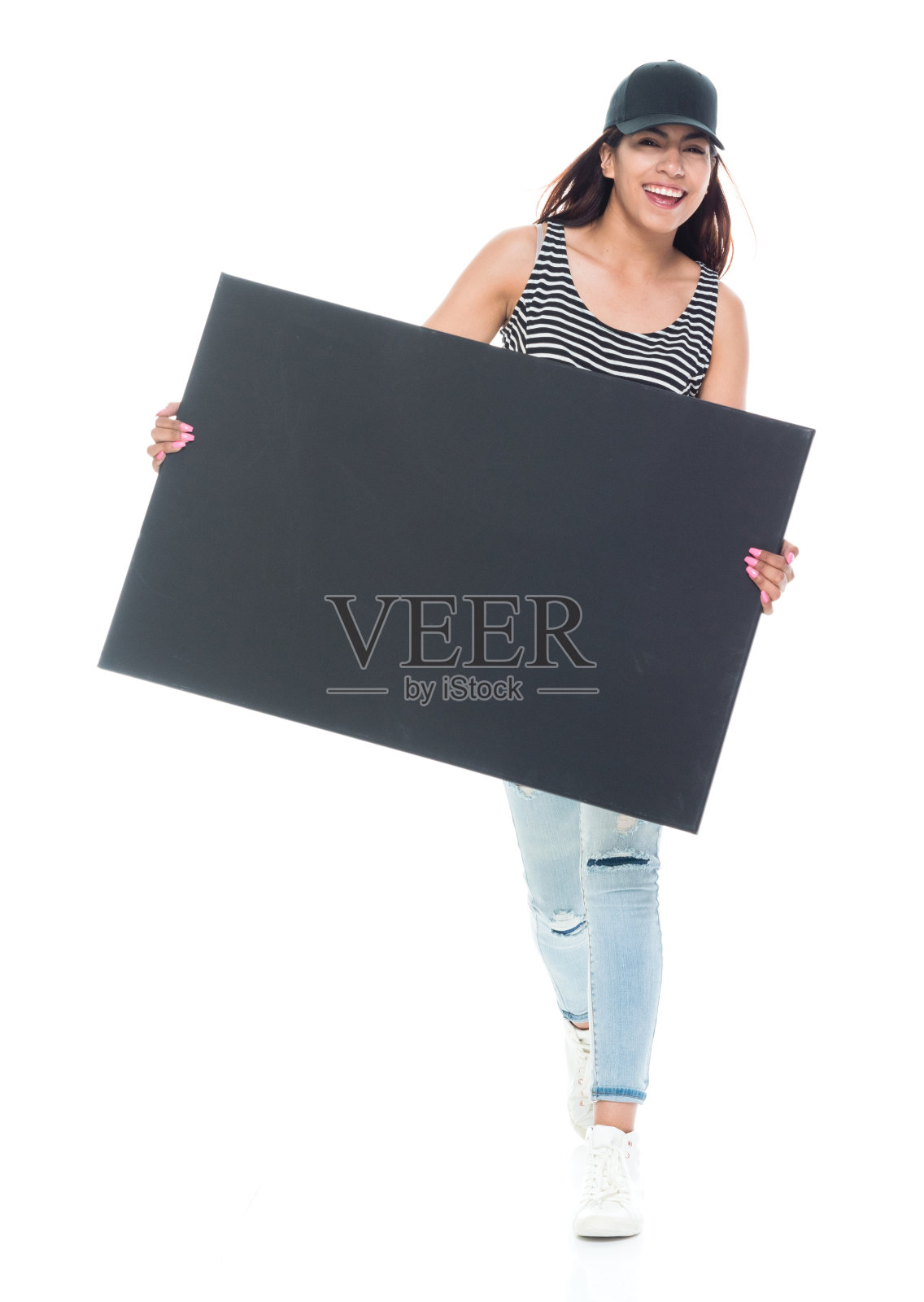 全长20-29岁美丽的拉丁美洲和西班牙裔的一个年轻女性只有/女性/年轻女性前面的白色背景穿着牛仔裤/背心/帽子/帽子谁是微笑/快乐/愉快的,拿着标志照片摄影图片