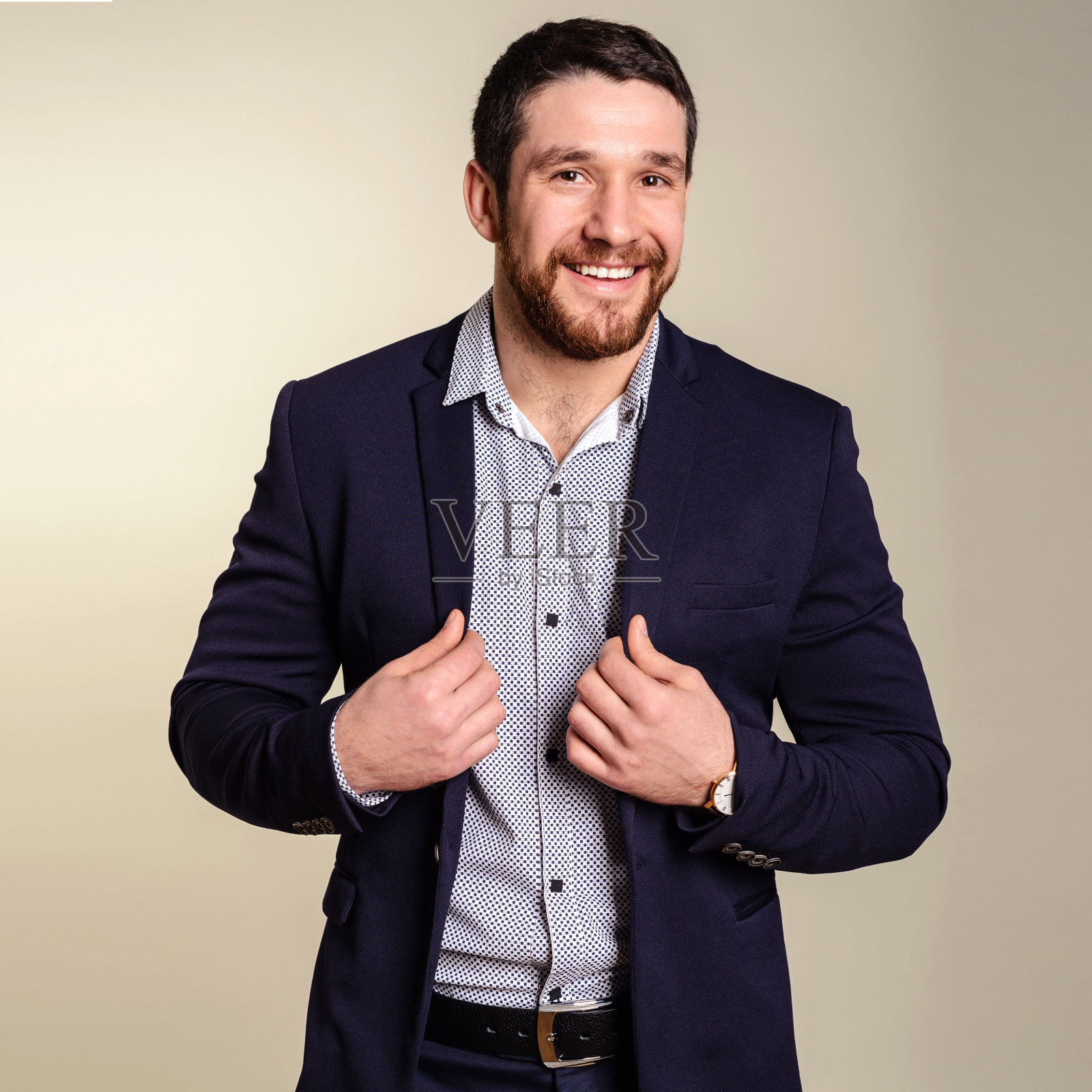 酷和时尚。留着胡子的英俊青年正整理着他的夹克,映衬着灰色的背景照片摄影图片