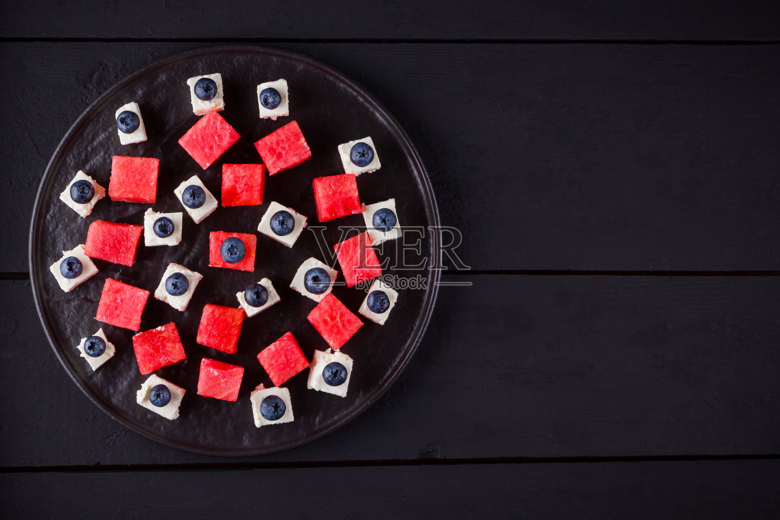 西瓜沙拉配羊乳酪。有蓝莓、西瓜和奶酪的健康沙拉。深色背景上的夏季沙拉。黑暗和喜怒无常照片摄影图片