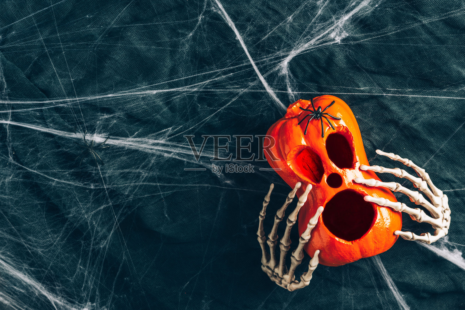 万圣节的背景,把南瓜的眼睛和嘴巴挖出来,瘦骨嶙峋的手抱着南瓜,杰克灯,阴沉而黑暗的气氛,拉长的网在背景照片摄影图片