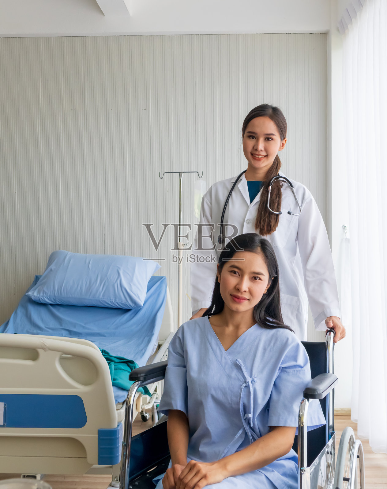 一位亚洲女医生在病房里为一位坐轮椅的女病人欢呼。照片摄影图片