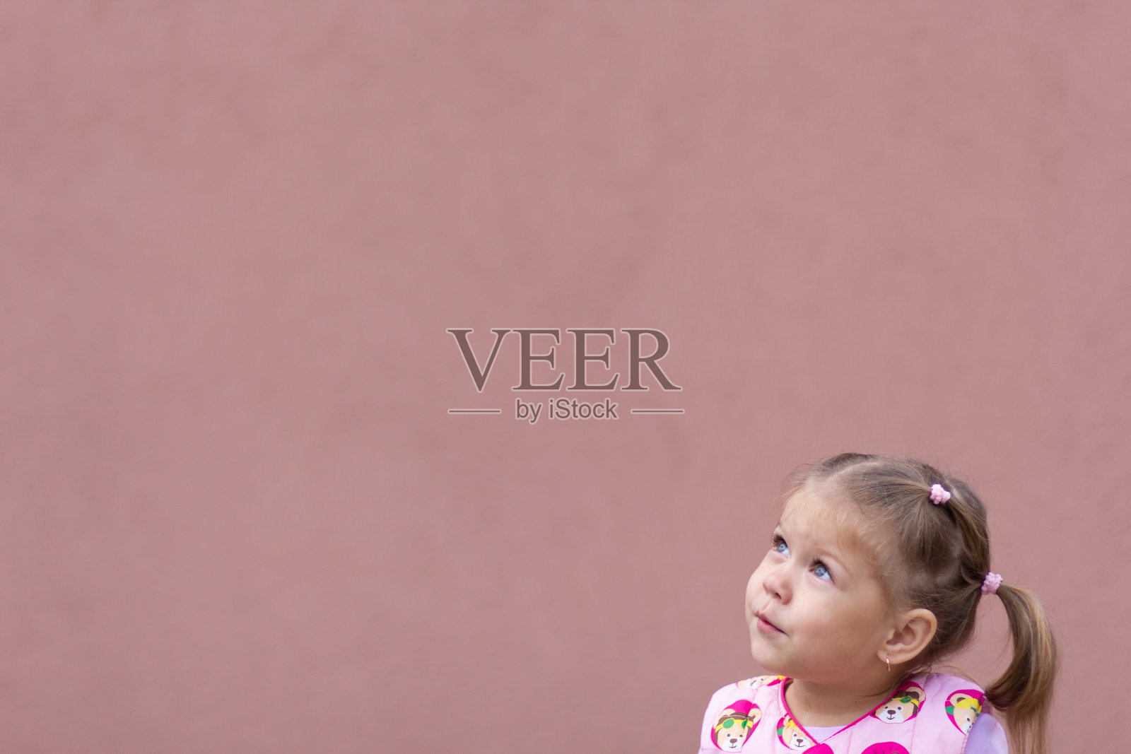 小女孩在粉色背景的角落里抬头看照片摄影图片