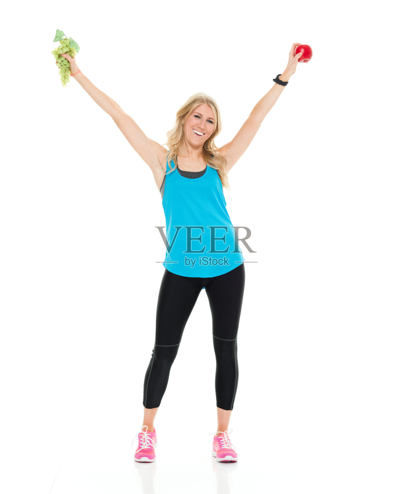 全长/一个20-29岁的成年人美丽的金发白人女性/年轻女性运动员/运动员站在白色背景谁是微笑/快乐/愉快的,展示手臂伸出和拿着水果照片摄影图片