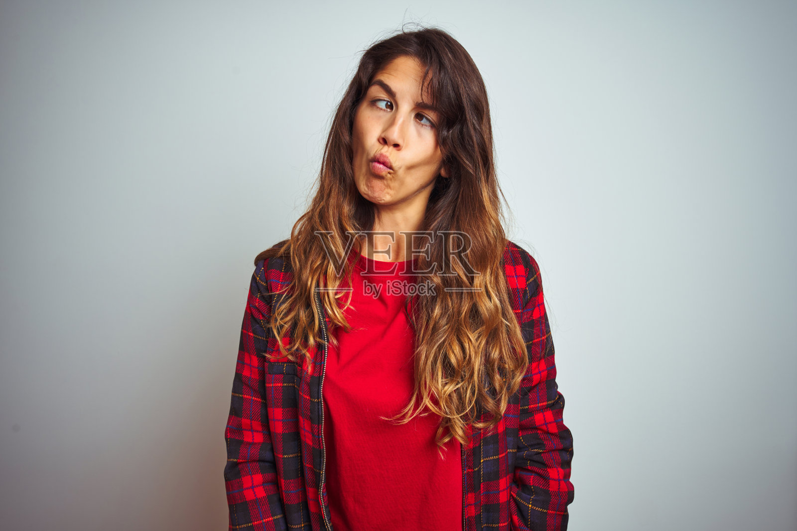 年轻美丽的女人穿着红色的t恤和夹克站在白色孤立的背景,使鱼的脸与嘴唇,疯狂和滑稽的手势。有趣的表情。照片摄影图片