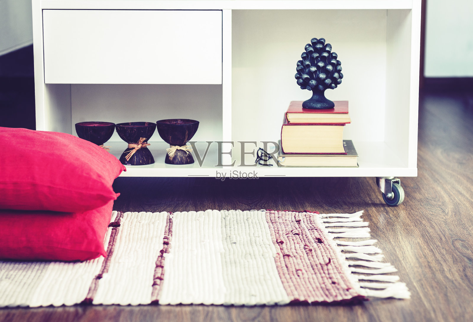 舒适的家庭内部装饰,燃烧的水疗香薰蜡烛椰子壳,金属花瓶,成堆的书,在白色玻璃床头柜附近的多色地毯装饰枕头背景照片摄影图片