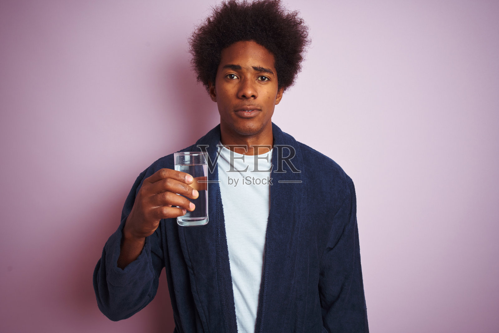 非裔美国人穿着睡衣,喝一杯水在孤立的粉红色背景与自信的表情在聪明的脸上思考严肃照片摄影图片