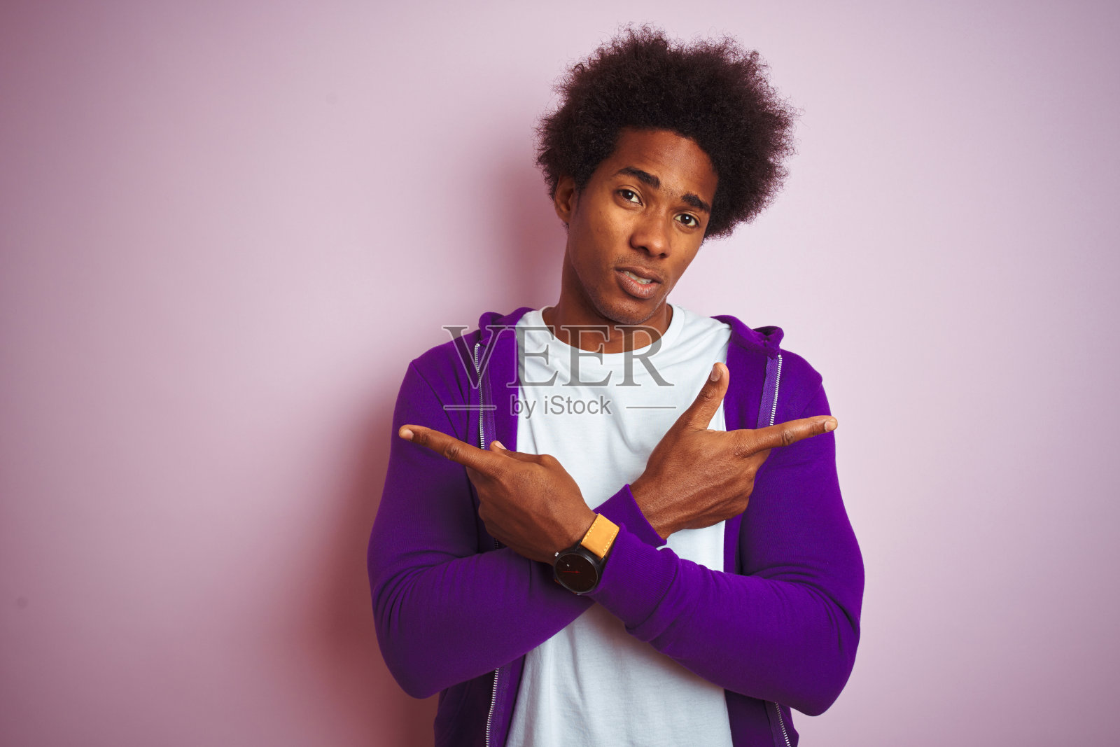 年轻的非裔美国人穿着紫色运动衫站在孤立的粉红色背景用手指指着两边,不同的方向不同意照片摄影图片