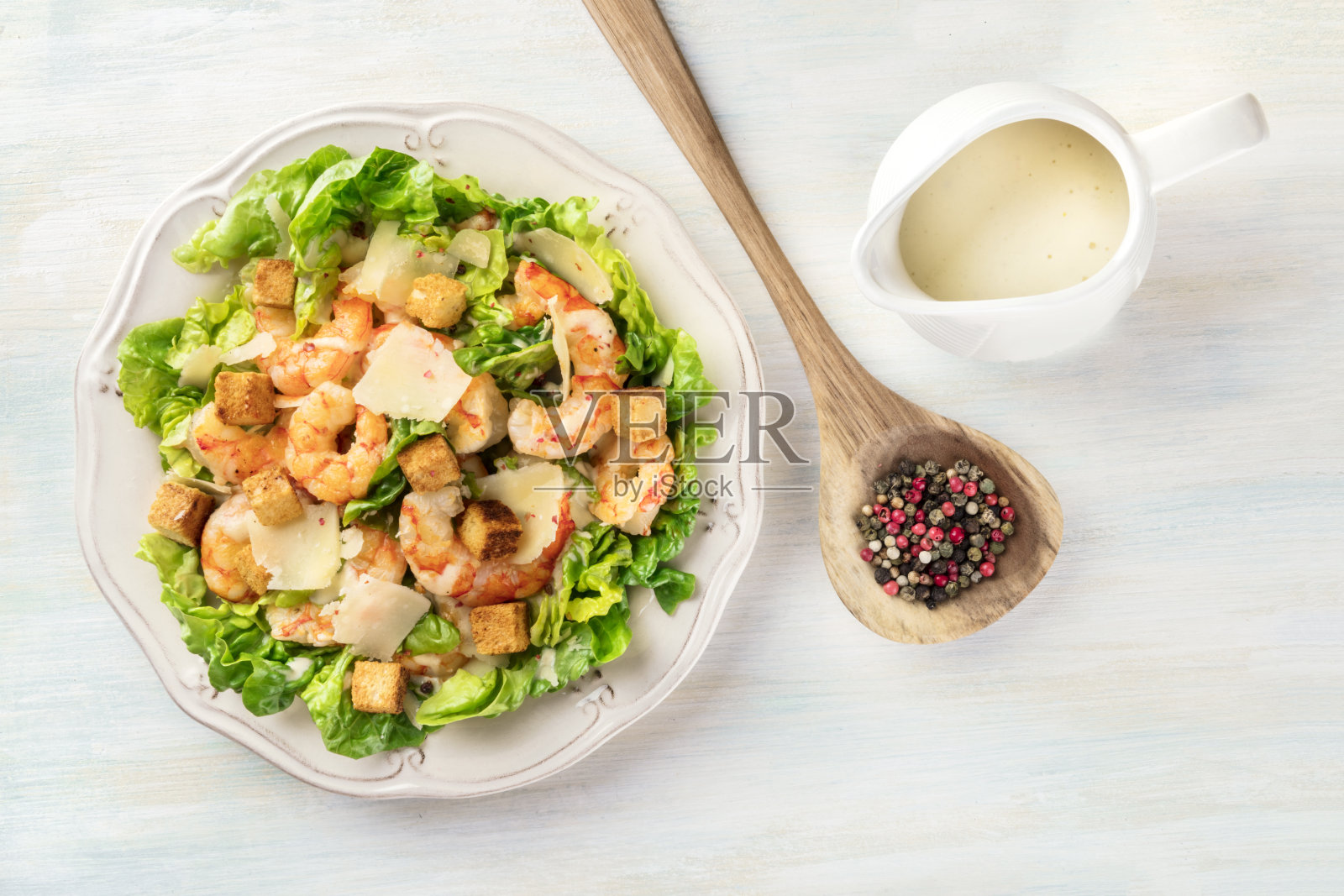 虾仁凯撒沙拉配上帕尔马干酪、油炸面包丁和生菜,酱汁装在卤盘里,顶部放上胡椒粒,还可以放上文字照片摄影图片
