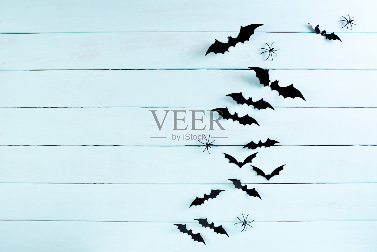 万圣节工艺品的顶视图,黑色的纸蝙蝠飞过蓝色的彩色木制背景与文本复制空间。万圣节的概念。照片摄影图片