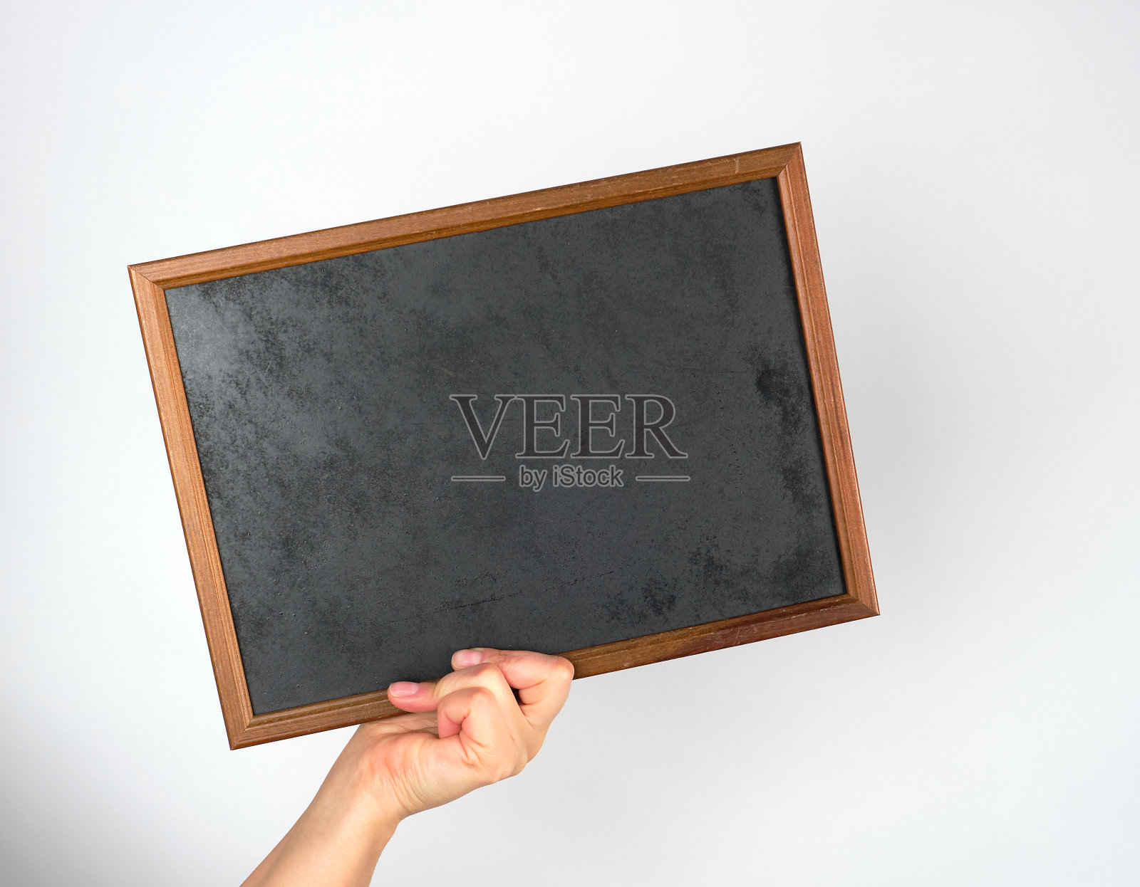 在灰色的背景上拿着一个空的木制粉笔框照片摄影图片