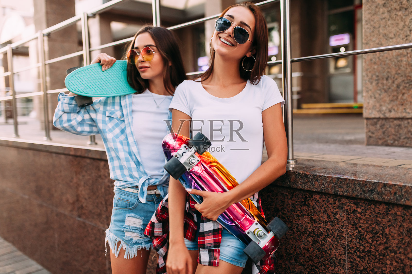 两个迷人的年轻女孩戴着太阳镜和滑板在城市里摆姿势照片摄影图片