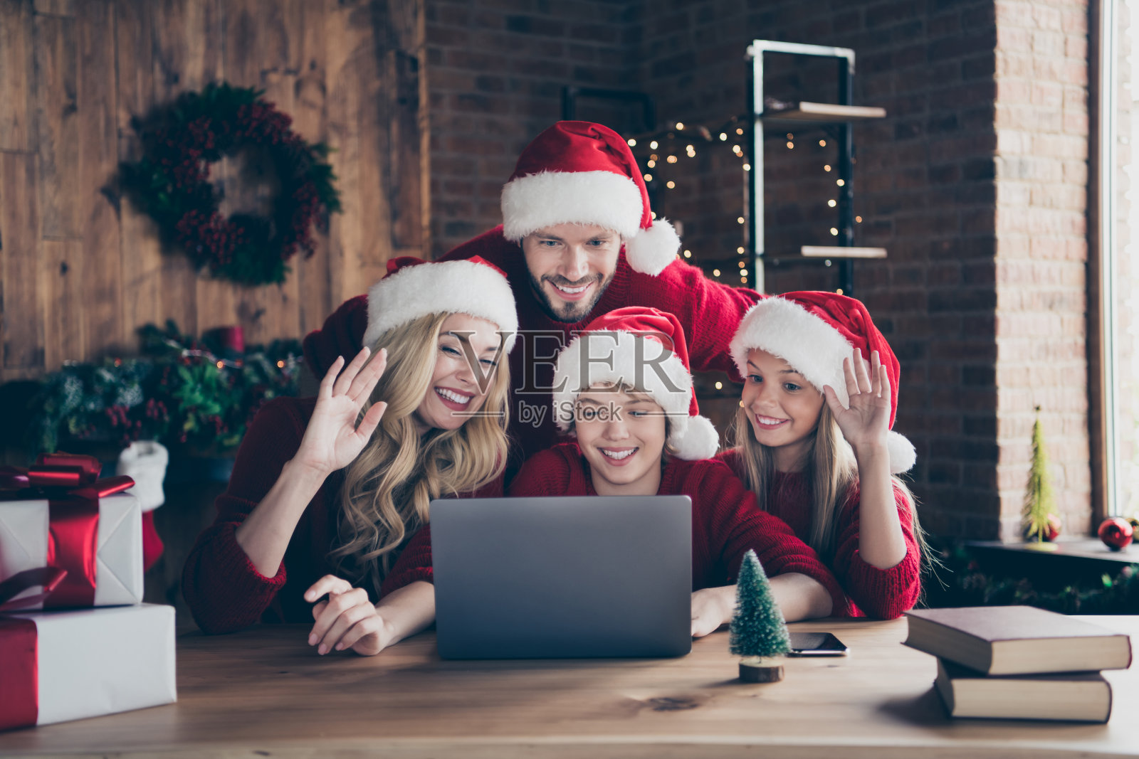 爸爸妈妈和两个孩子的照片制作圣诞前夕skype视频会议会议挥舞手臂祝贺亲戚坐在室内戴红色毛衣圣诞老人帽照片摄影图片
