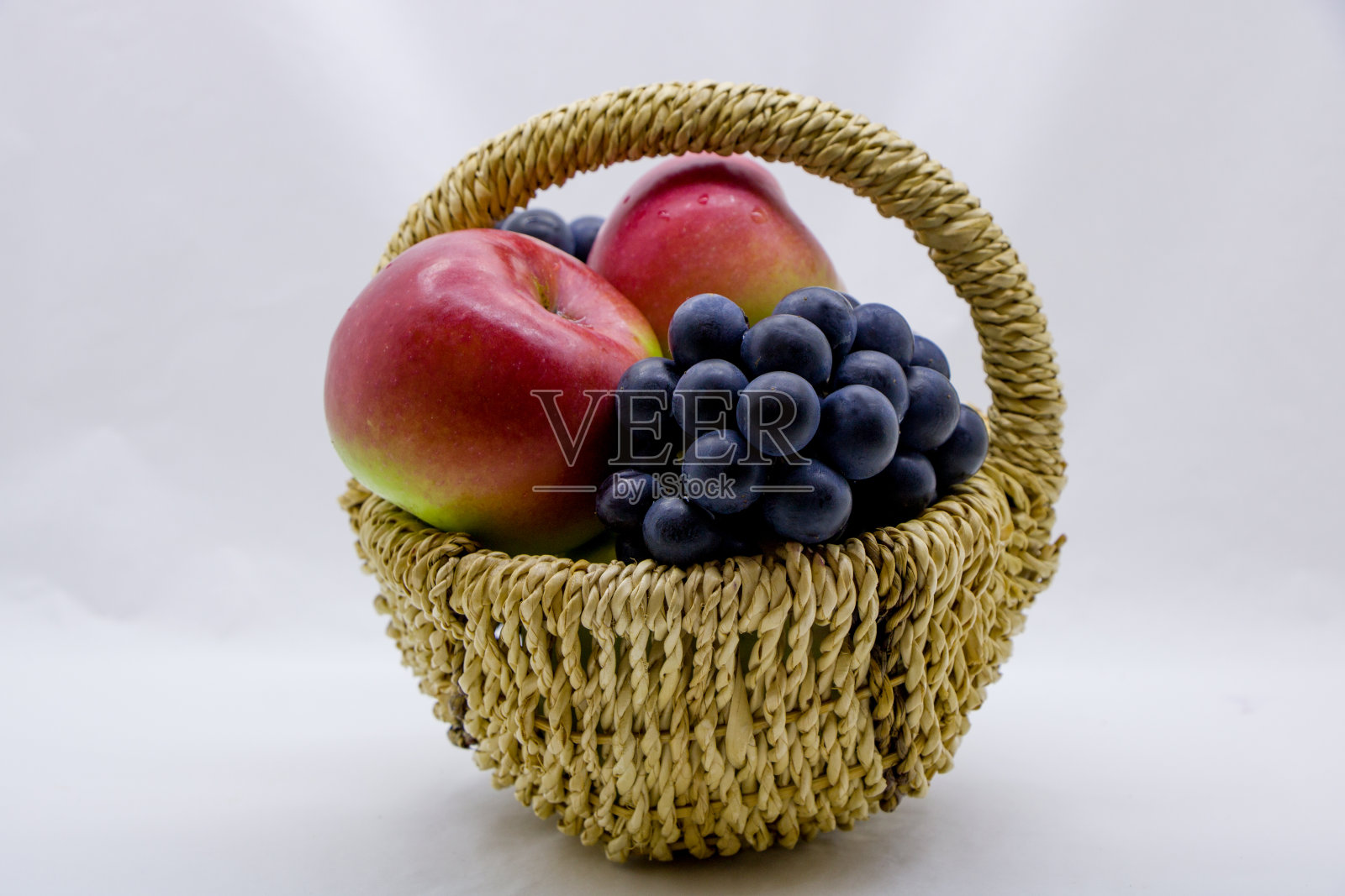 篮子里的苹果和葡萄,背景是白色。照片摄影图片