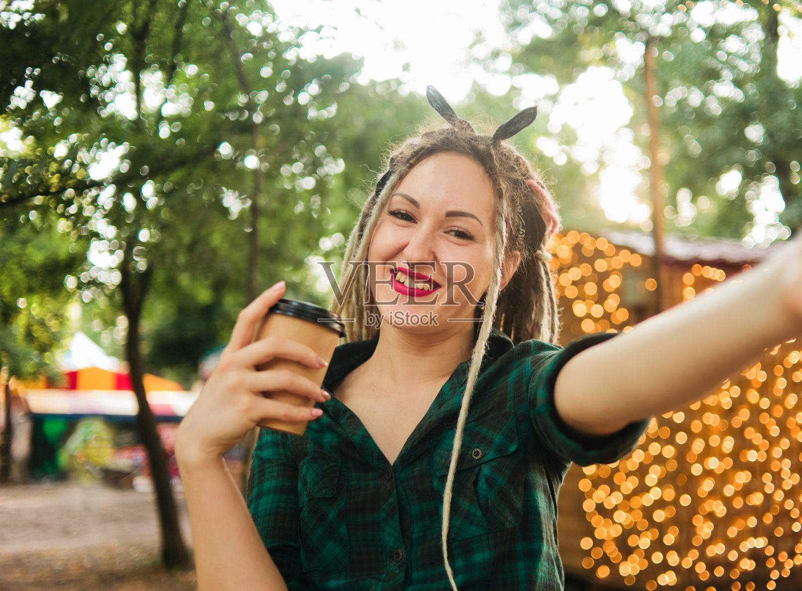 有魅力的女人与一个非正式的发型雷鬼发自拍肖像和拿着一杯咖啡的背景在晚上的花环照片摄影图片