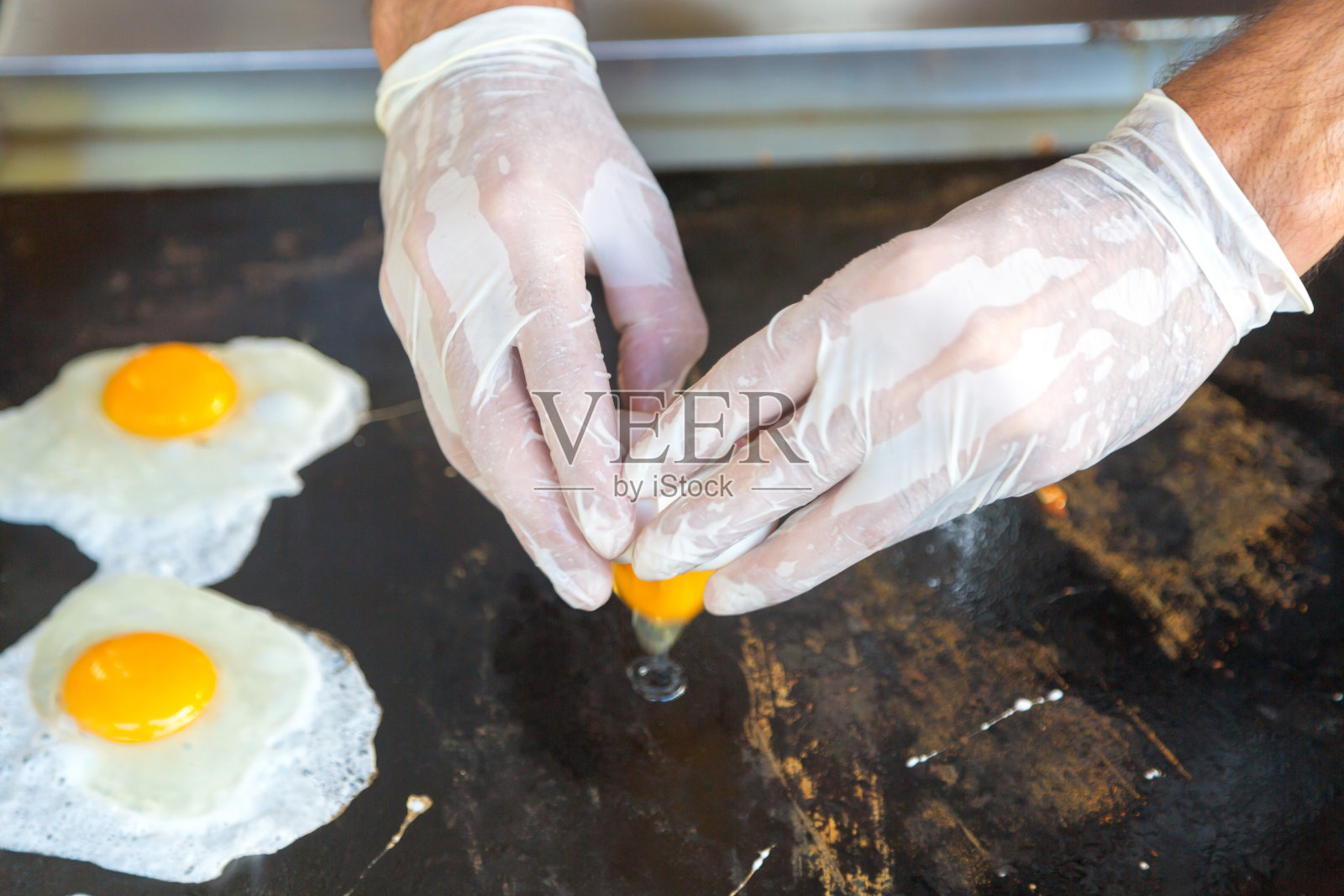 一个戴白手套的男人煎鸡蛋。照片摄影图片