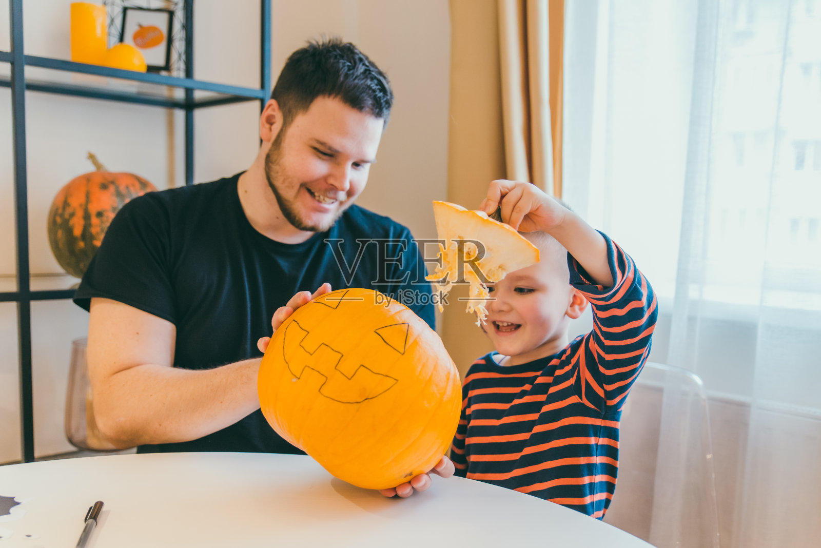 年轻的父亲和蹒跚学步的儿子使杰克南瓜头万圣节假期照片摄影图片