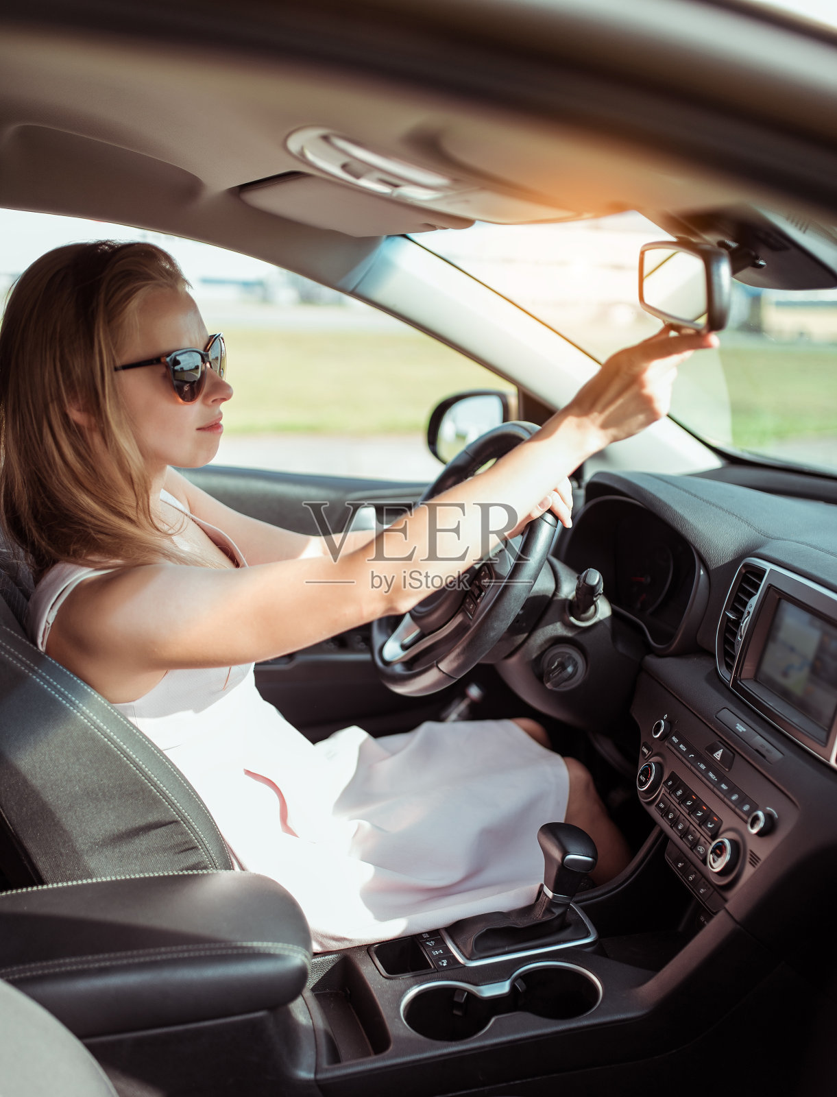 女孩女人在车里,在夏天的城市,看后视镜,停车场,看后排座位的孩子和孩子,开心地笑在太阳镜。粉色连衣裙,自动变速箱。照片摄影图片