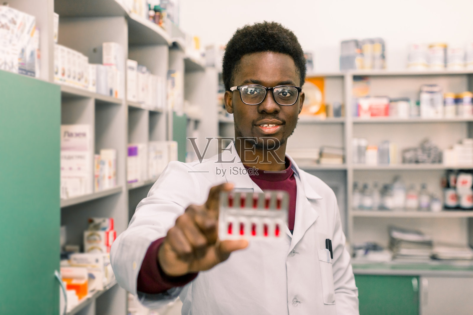 年轻的非洲裔美国男子药剂师手里拿着红色药丸泡站在现代药房的内部照片摄影图片