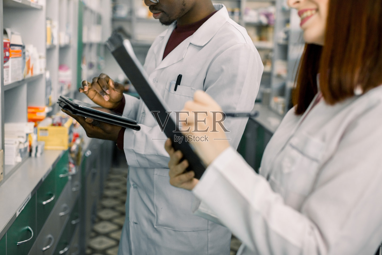 非洲男子药剂师在分销公司使用数字药片下订单,而他的女同事在剪贴板上做笔记。在药房工作。药店内部,药店照片摄影图片