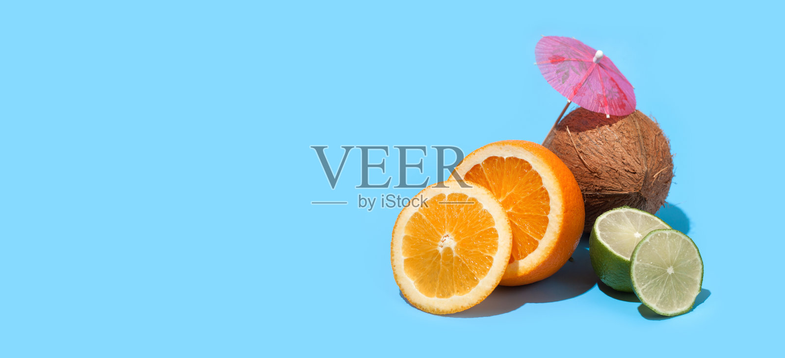 新鲜多汁的橙子,椰子和青柠与鸡尾酒伞孤立在蓝色的背景。健康饮食和节食的概念。旅游和假日概念。副本的空间。为你的文本留出空间照片摄影图片