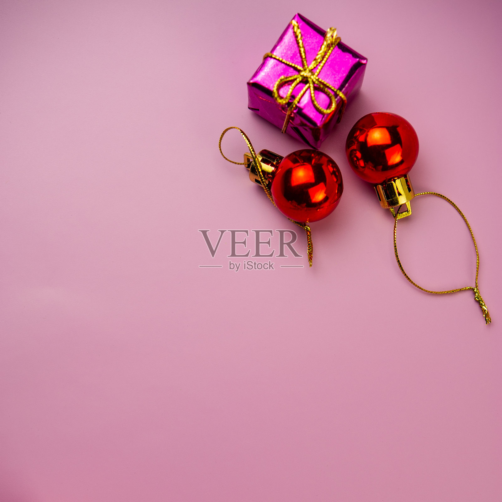 紫色的礼盒和两个红色的圣诞球,粉红色的背景上有一根金色的绳子。照片摄影图片