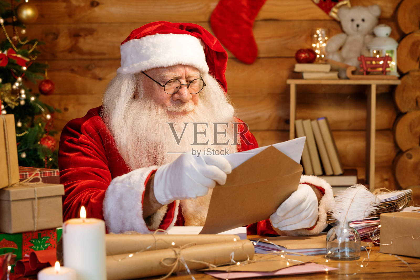 严肃的圣诞老人坐在家里的桌子旁,把信放进信封里照片摄影图片