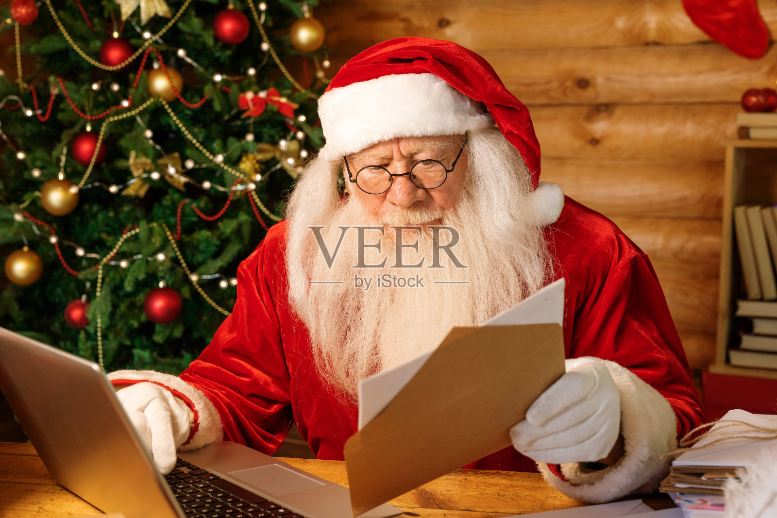 圣诞老人拿着信封看着地址,然后把它放进笔记本电脑里照片摄影图片