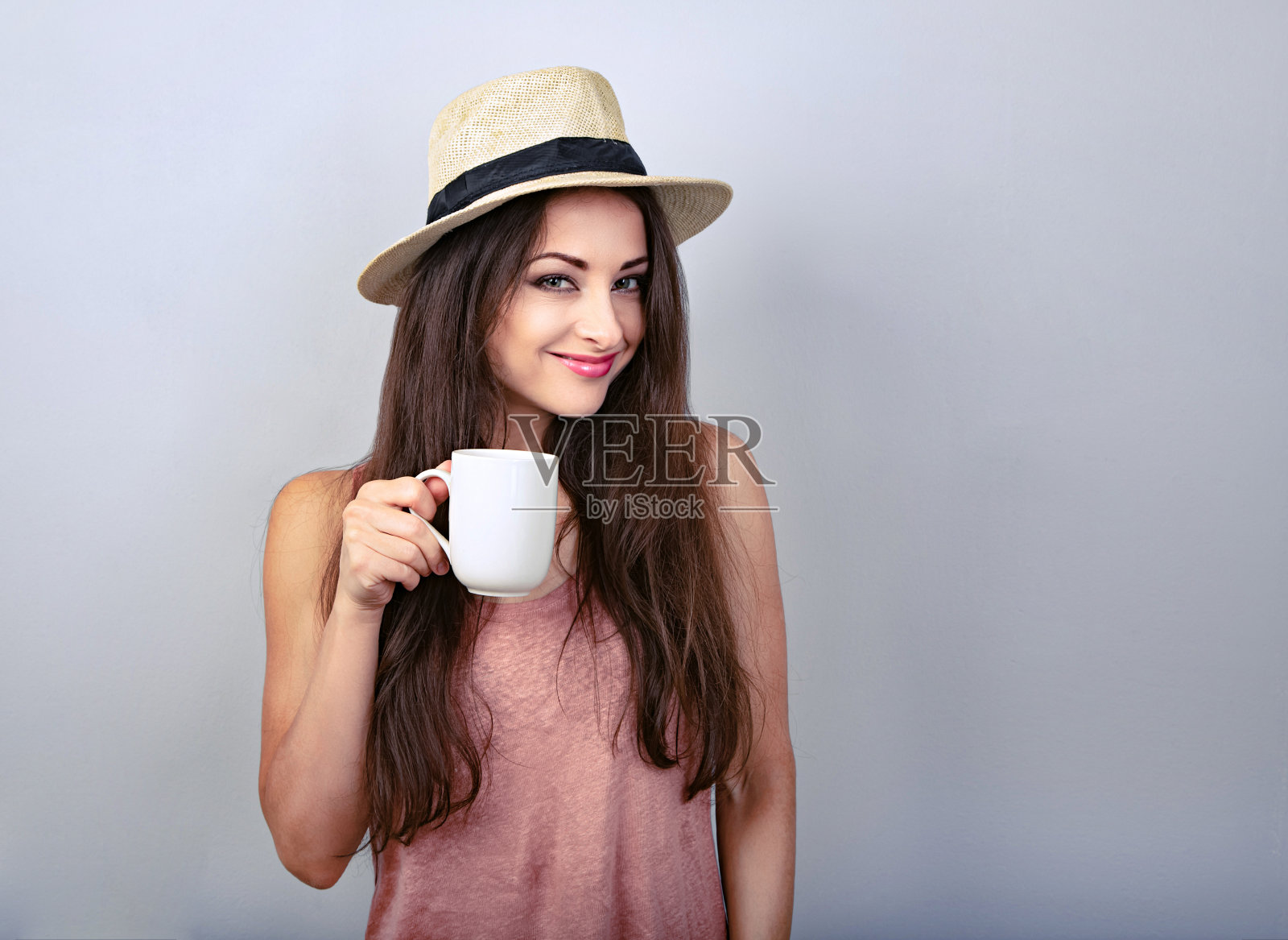 微笑随意的年轻女子与一杯咖啡看起来快乐的草帽在蓝色的背景照片摄影图片