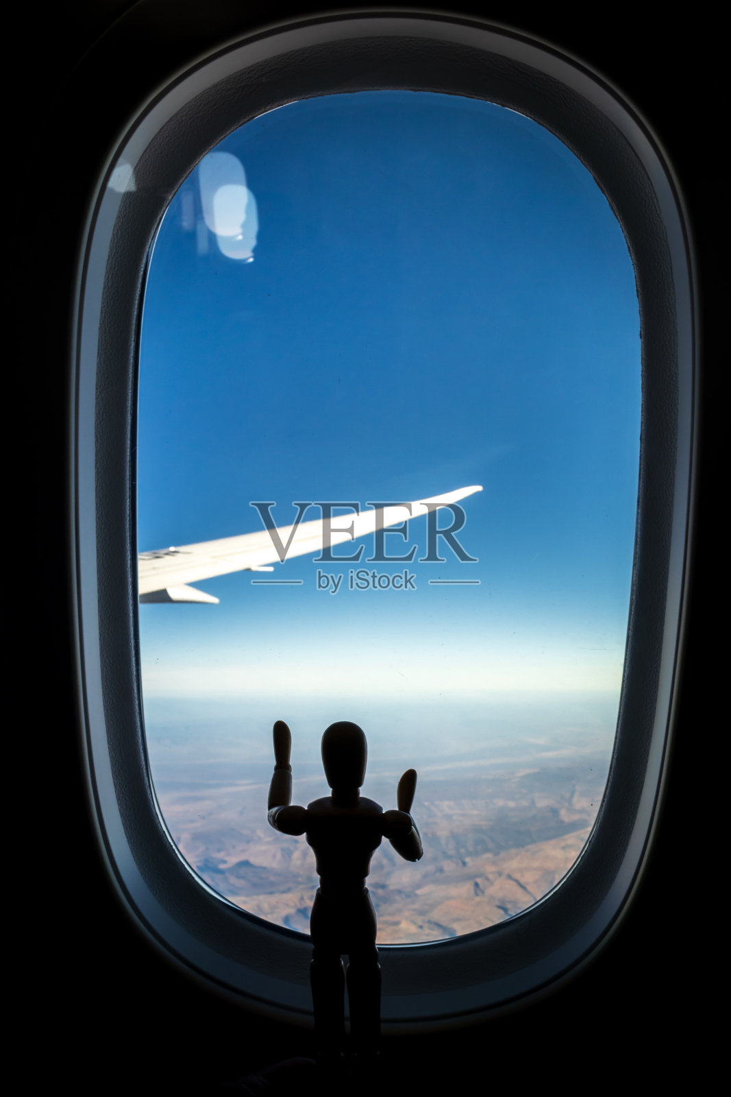 一个木制人体模型站在飞机窗外看着下面的风景照片摄影图片