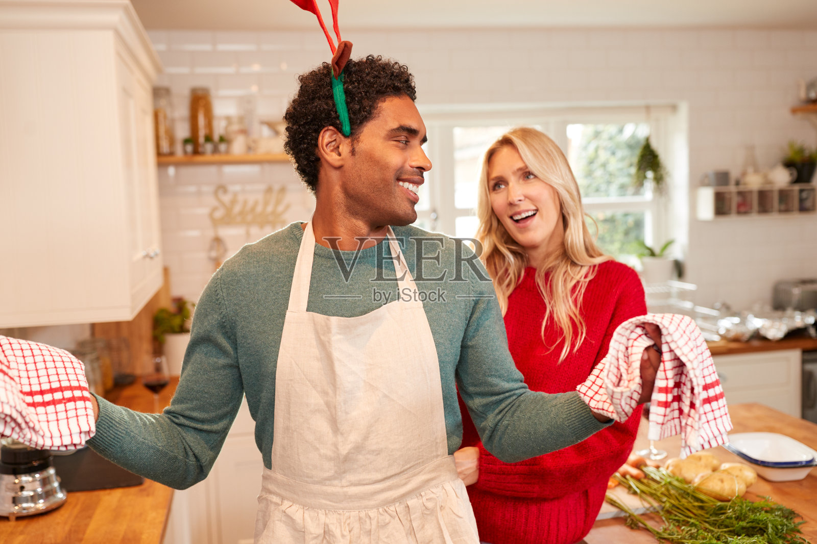圣诞节当天,一对夫妇在厨房里准备晚餐时戴着鹿角照片摄影图片