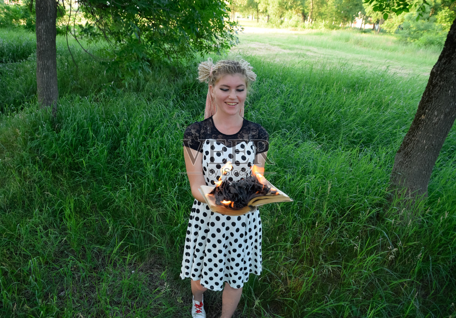 女孩手里拿着一本燃烧着的书。一个年轻的女人在森林里烧了一本书。照片摄影图片