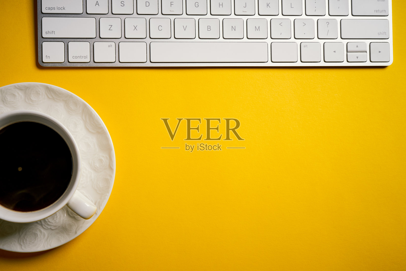俯视图白色键盘和一杯咖啡在黄色的桌子上照片摄影图片